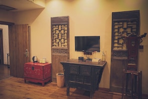 A room with a wooden cabinet, a television mounted on the wall, and a traditional decorative screen. - QingXi Hotel (Xiangxi)
