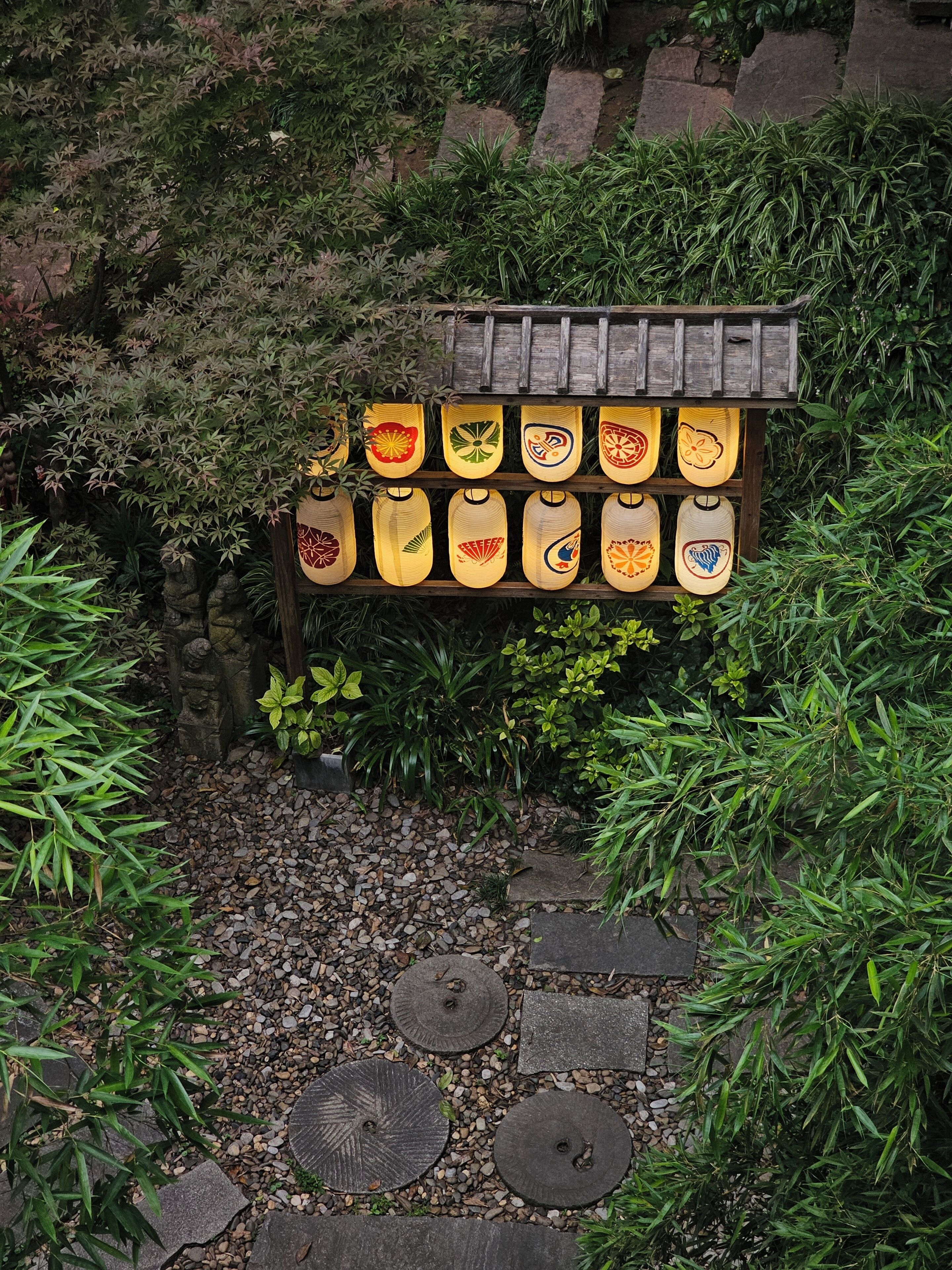 A garden pathway with stone slabs and a wooden structure displaying lanterns.
