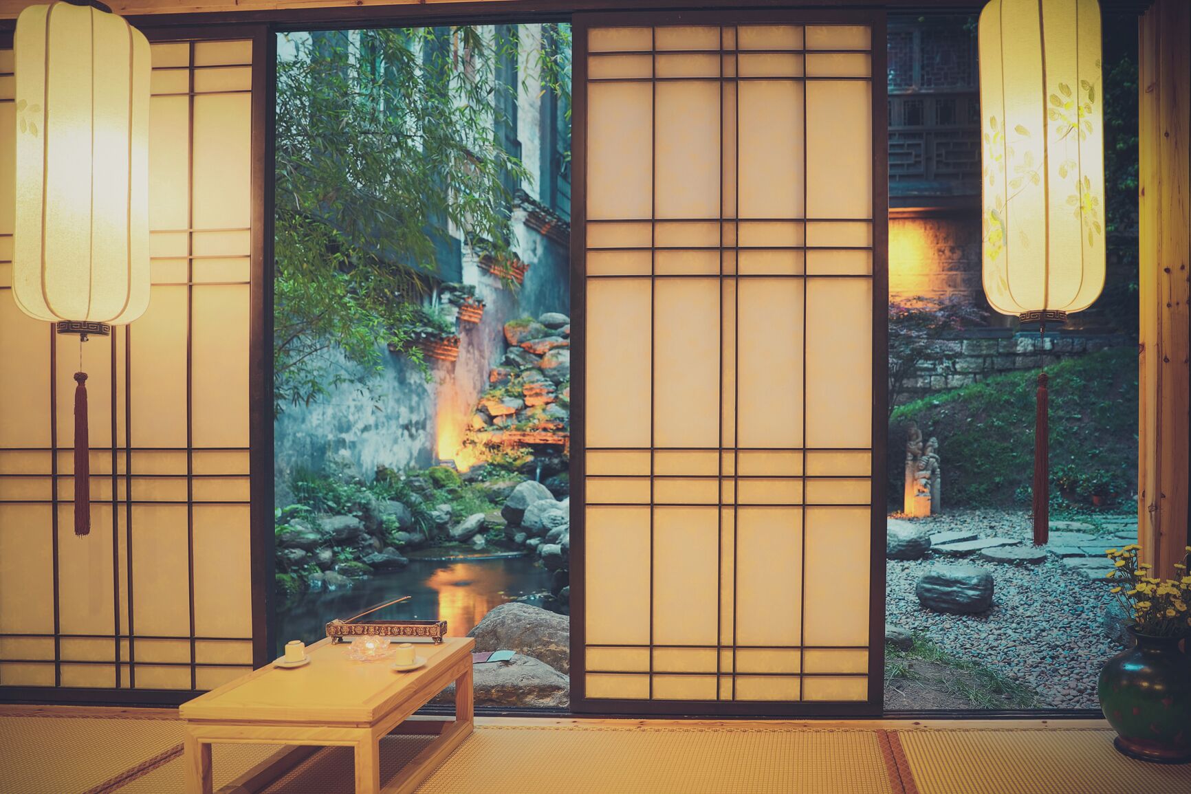 A traditional Japanese room with tatami flooring, a low table, and sliding doors with a view of a garden.
