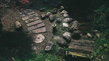 Un sendero de piedra con escalones que conducen a un puente de madera sobre un cuerpo de agua, rodeado de rocas y follaje.