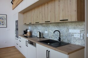 A modern kitchen with wooden cabinets, a marble backsplash, a black sink, and a built-in dishwasher. - Modern wooden cottage with panoramic views, a large terrace, and air conditioning (Roznov pod Radhostem)