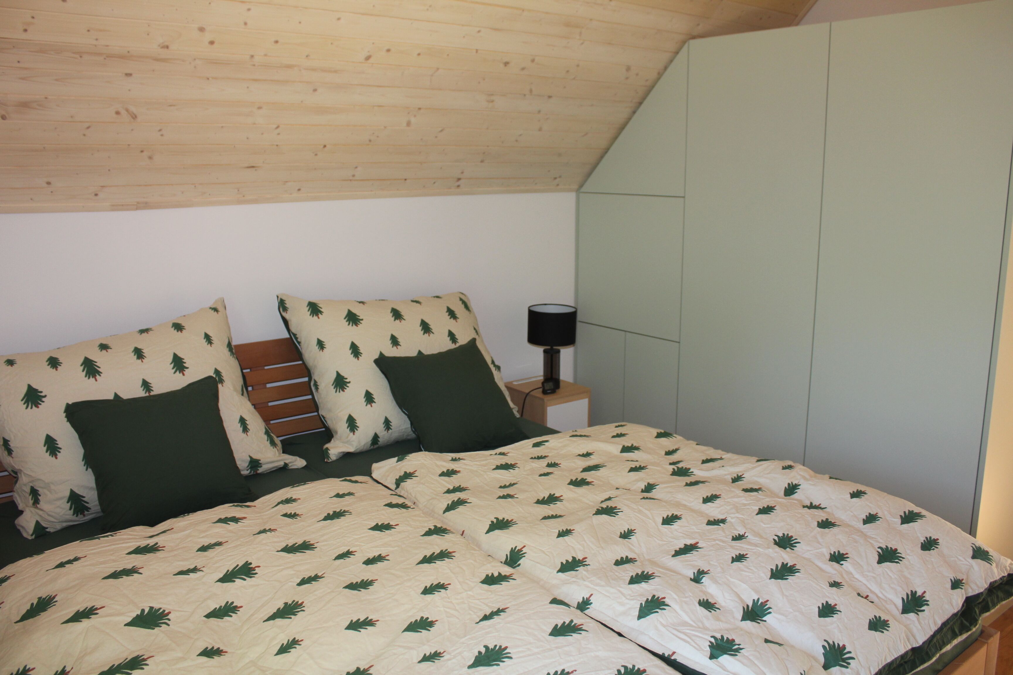 Une chambre avec un plafond en pente, un lit recouvert d’une couvre-lit à motifs, deux oreillers, une lampe de chevet et une table de chevet.