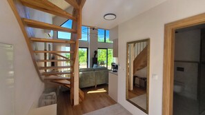 A modern interior with a wooden staircase, a large mirror, and a view through a window.