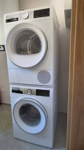 A stacked washer and dryer unit with a control panel, a vent, and a door. - Modern wooden cottage with panoramic views, a large terrace, and air conditioning (Roznov pod Radhostem)