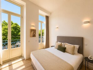 A bedroom with a large bed, a balcony with a railing, and a view of greenery outside. - MyStay Ribeira Hotel (Porto)