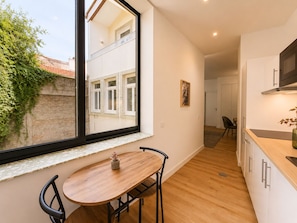 A modern kitchen with a large window, wooden flooring, and a dining area with a table and chairs.