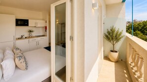 Un balcón con planta en maceta, cama con almohadas, zona de cocina y vista panorámica de la ciudad.