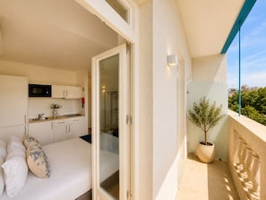 A balcony with a potted plant, a bed with pillows, a kitchen area, and a view of the cityscape.