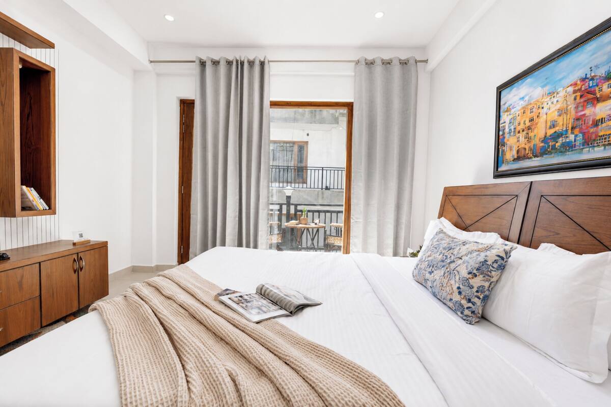 A hotel room with a bed, a wooden headboard, a painting, a balcony view, and a wooden wardrobe.