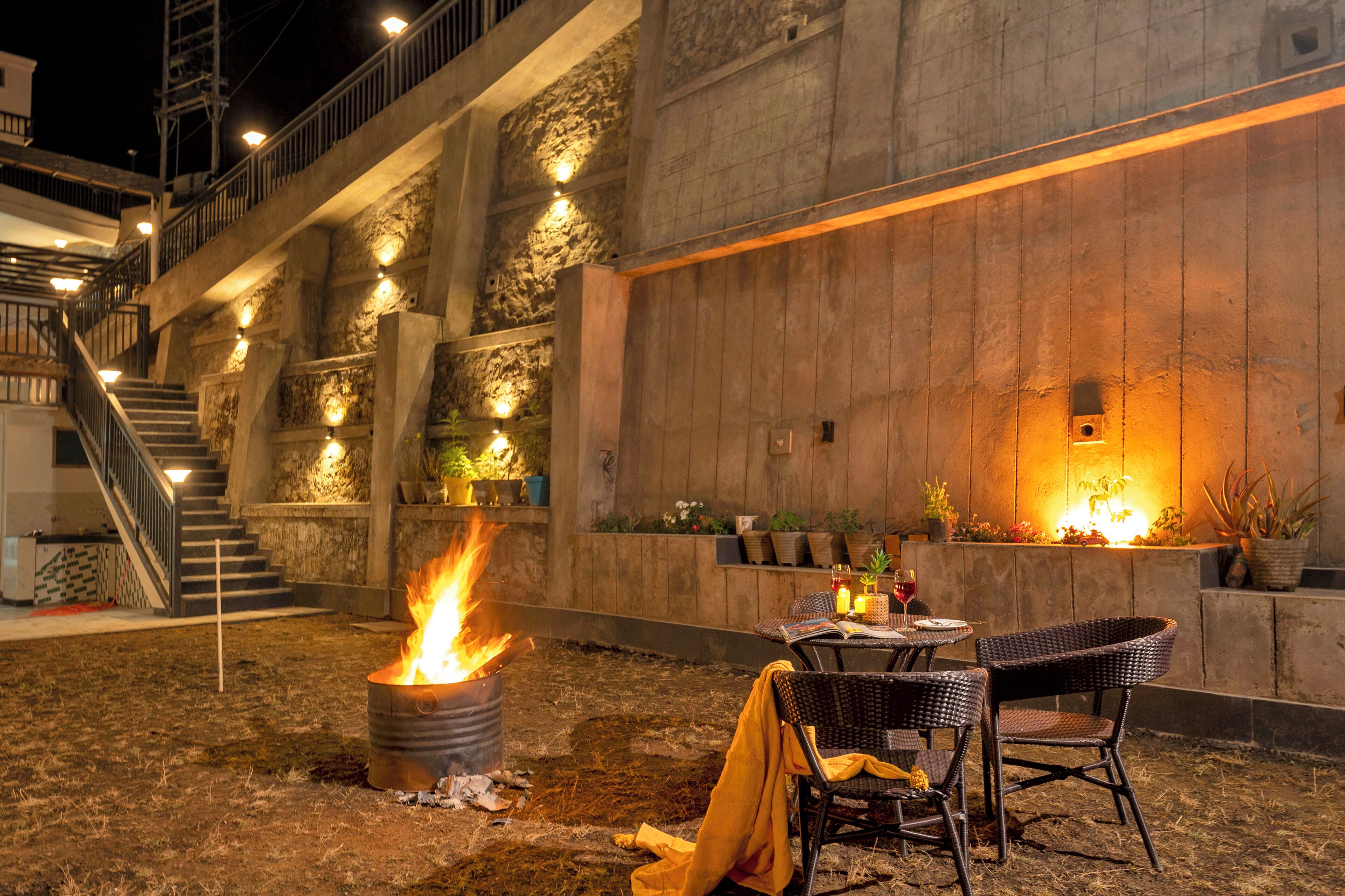 An outdoor dining area with a fire feature, wicker chairs, and a staircase leading to an upper level.
