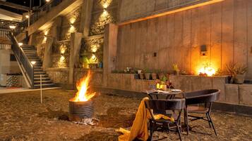 An outdoor dining area with a fire feature, wicker chairs, and a staircase leading to an upper level.
