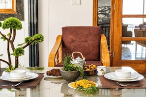 Mesa de jantar com pratos, tigelas e uma cadeira em um quarto com janela e planta.