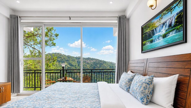 A bedroom with a large bed, a view of a balcony, and a painting of a waterfall. - Mist & Manor Petfriendly Apartments (Dilman)