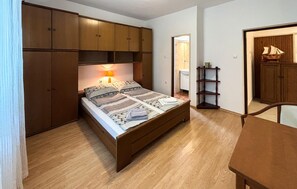 A bedroom with a wooden bed, a bedside lamp, a wooden wardrobe, and a small table. - 2 bedroom nice apartment in Supetarska Draga (Supetarska Draga)