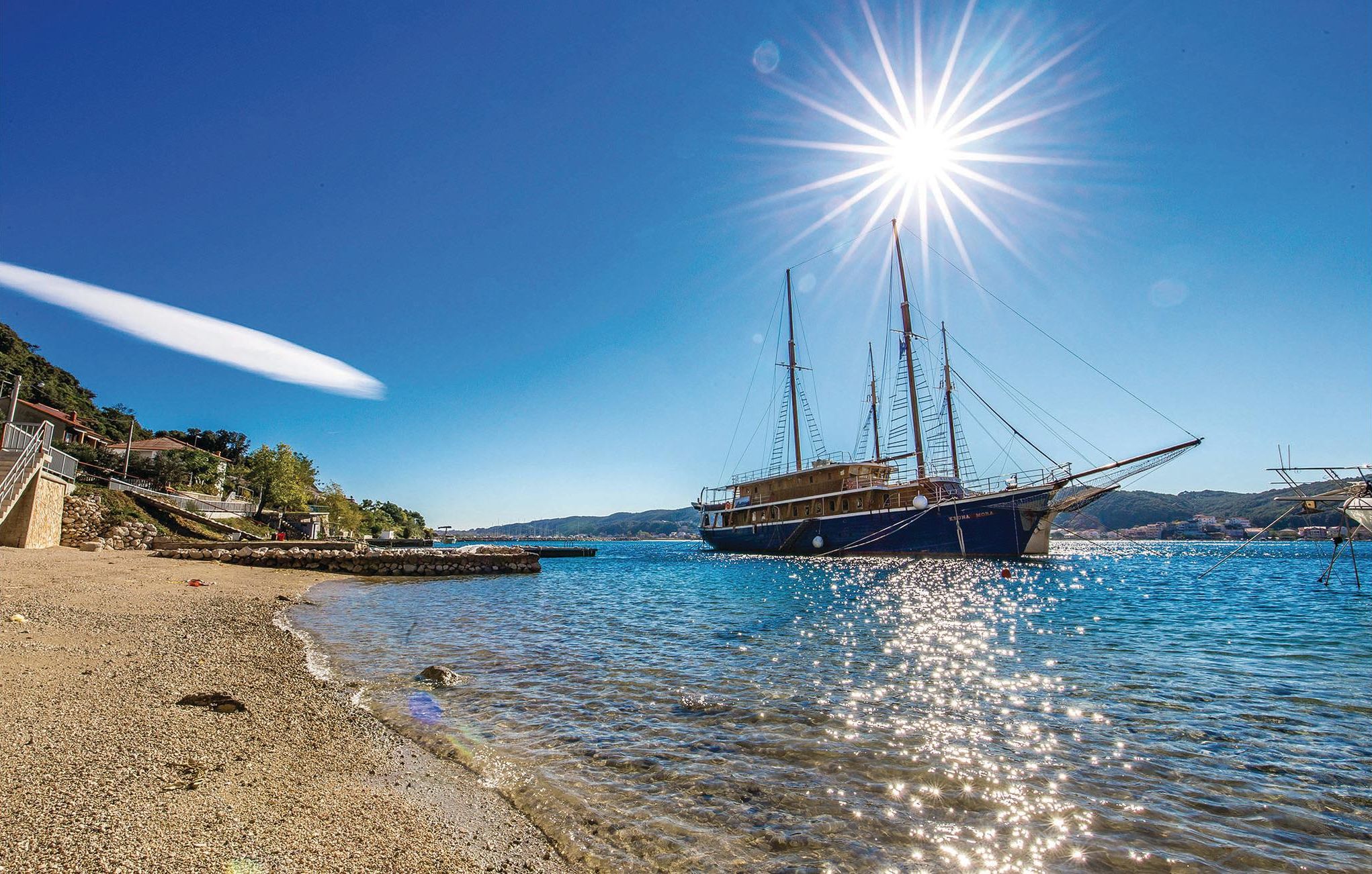 Un paysage côtier avec un bateau amarré à un quai, une eau bleue et limpide, et une plage rocheuse.
