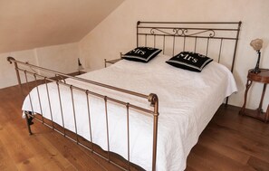 Ein Bett mit Metallgestell, weißer Bettwäsche und zwei Kissen mit der Aufschrift 'Frau' und 'Herr'.