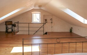 Ein Dachzimmer mit Holzboden, Metallgeländer, einem Fenster und einer Tür.