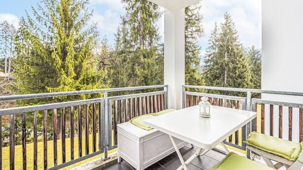 Un balcone con un tavolo bianco e due sedie, una lanterna e vista sugli alberi.