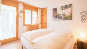 Una camera da letto con un letto, una cassettiera, una finestra con tende, un quadro appeso al muro e una decorazione a forma di cuore.