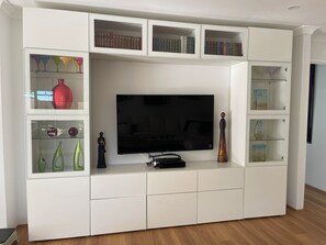 Un salon moderne doté d’un téléviseur à écran plat, d’étagères intégrées où sont disposés des livres et des objets décoratifs, et présentant un design minimaliste.