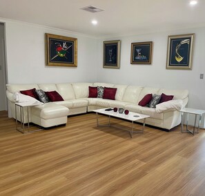 Un salon avec un canapé d’angle en cuir blanc, une table basse blanche et trois œuvres d’art encadrées accrochées au mur.
