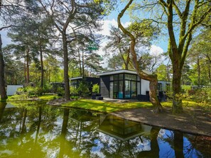 Ein modernes Haus mit Wintergarten, umgeben von einem Teich und Bäumen.