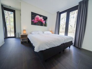 Ein modernes Schlafzimmer mit einem großen Bett, einem Nachttisch, einem Wandbild und Blick durch das Fenster.