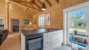Een houten hut interieur met een kookeiland, een eethoek en een groot raam met uitzicht op de natuur.