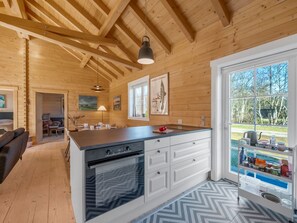 Ein Holzblockhaus-Interieur mit Kücheninsel, Essbereich und großem Fenster mit Blick ins Freie.