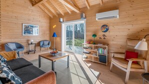 Een houten interieur met een bank, stoelen, een tafel, een boekenkast en uitzicht door een glazen deur.
