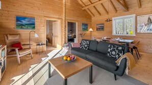 Een houten chalet van binnen met een bank, een eettafel, een lamp en een schilderij aan de muur.