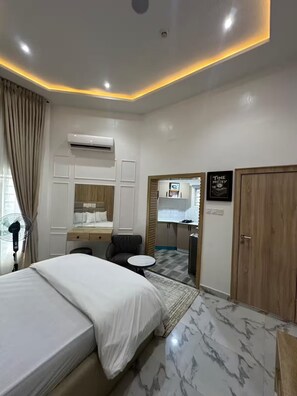 A hotel room with a bed, a desk, a chair, a small table, an air conditioning unit, and a wardrobe. - 4bedroom Luxury Apartment (Lagos)
