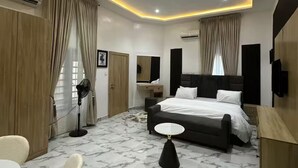 Ett modernt hotellrum med en säng, ett skrivbord, en stol, en fläkt och en TV.