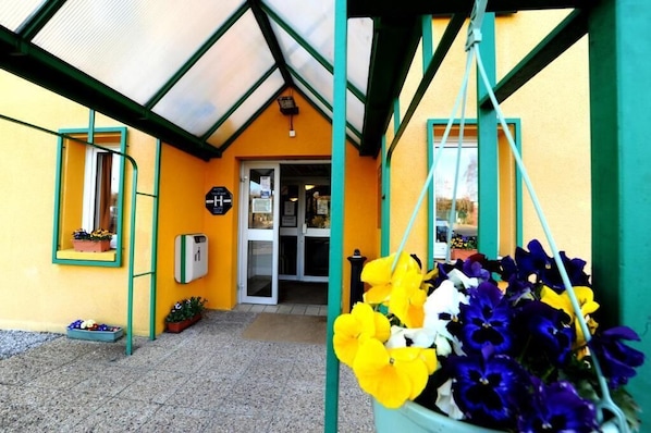 A building entrance with a glass door, a green-framed window, and a hanging flower basket. - Welcomotel (Limoges)
