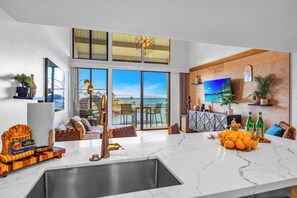 Ein modernes Wohnzimmer mit großem Fenster zum Meer, eine Küche mit Marmorarbeitsplatte und ein Essbereich mit Aussicht.
