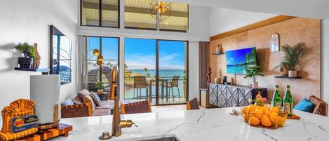 A modern living room with a large window overlooking the sea, a kitchen with a marble countertop, and a dining area with a view.