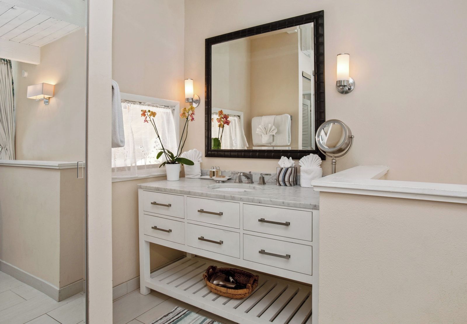 Une salle de bain avec un meuble-lavabo blanc, un grand miroir, une orchidée en pot et un porte-serviettes.