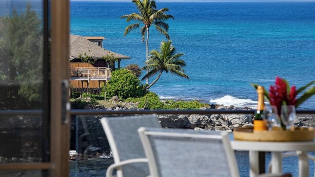 A coastal view with a house, palm trees, and a table with a bottle and flowers. - Napili Point 2 Oceanfront Villas, Sleeps 8 | Car Incl. w/ 6 nights | ML-4106 by KBM (Lahaina)