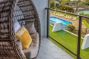 Ein Korbstuhl mit Kissen, Blick auf Pool und Rasen sowie ein Balkongeländer.