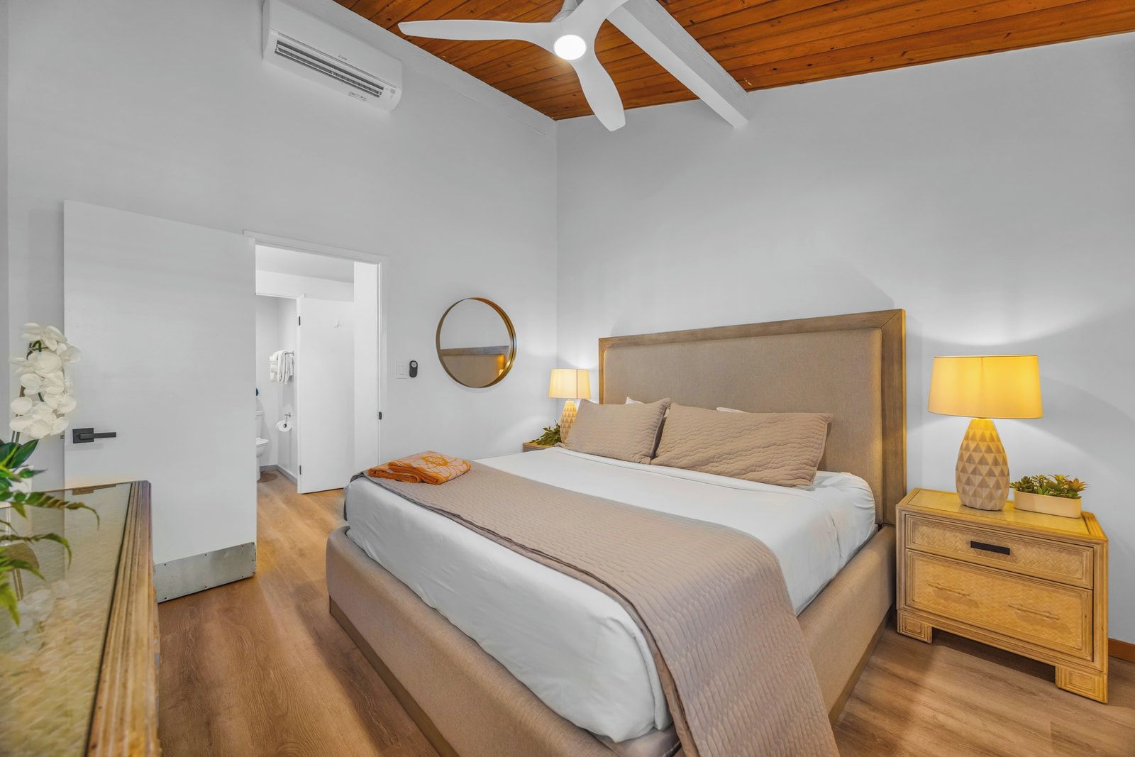 A bedroom with a bed, bedside tables, a mirror, and a ceiling fan.