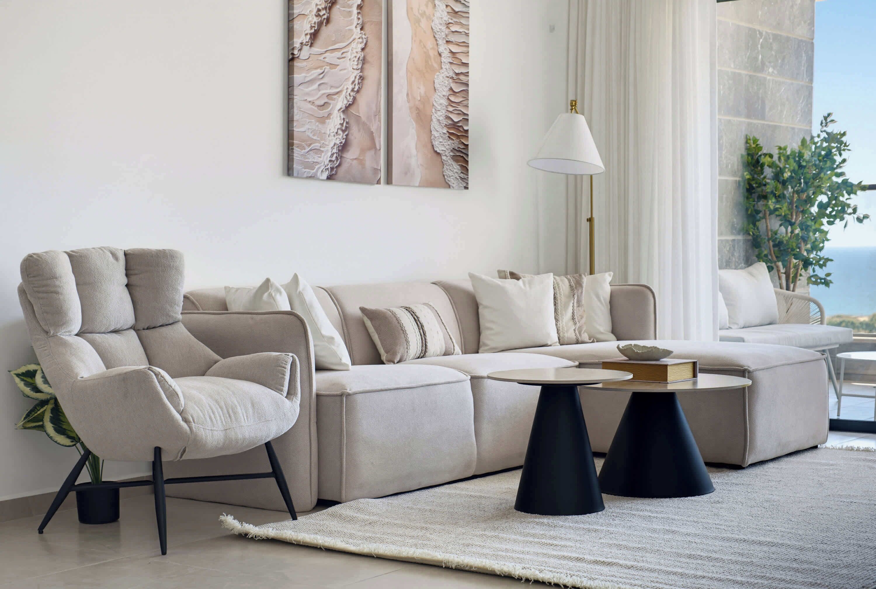 Un salon moderne avec un canapé d’angle, une table basse ronde et une grande fenêtre offrant une belle vue.
