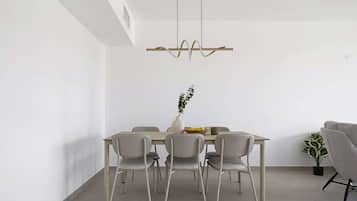 Een moderne eetruimte met een rechthoekige tafel, zes stoelen, een vaas met een plant en een hanglamp.