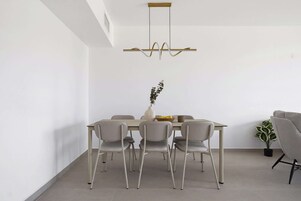 Uma sala de jantar moderna com uma mesa retangular, seis cadeiras, um vaso com planta e um lustre.