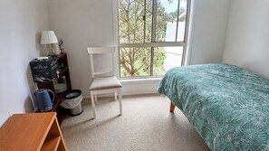 Ein Schlafzimmer mit Bett, Sessel, kleinem Tisch, Fenster und Heizkörper.