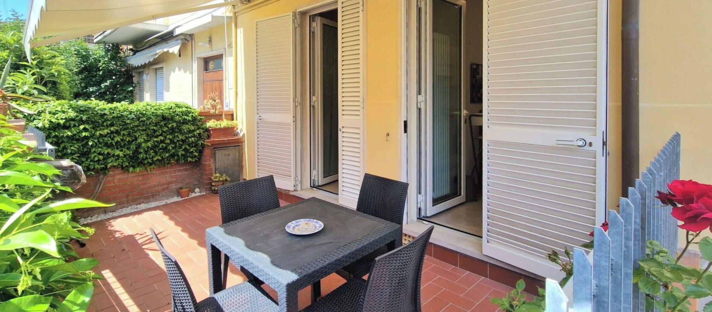 A patio with a table and chairs, a sliding door, and a hedge.