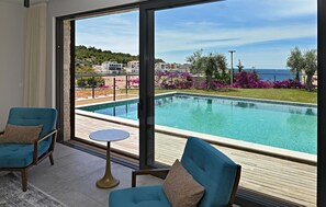 A room with a large window, a pool, and two blue chairs. - Awesome home in Primosten (Primosten)