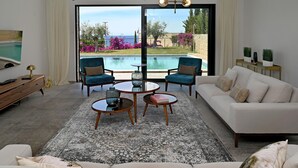 Una sala de estar moderna con vista a una piscina, dos sillones, un sofá y un televisor.