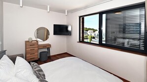Un dormitorio con cama, cómoda, espejo, televisor y ventana con persianas.