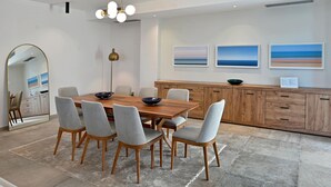 Un comedor moderno con una mesa de madera, sillas grises, un espejo grande y una lámpara colgante.