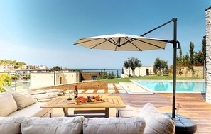 Uma área à beira da piscina com um deck de madeira, móveis de exterior e vista para o mar.